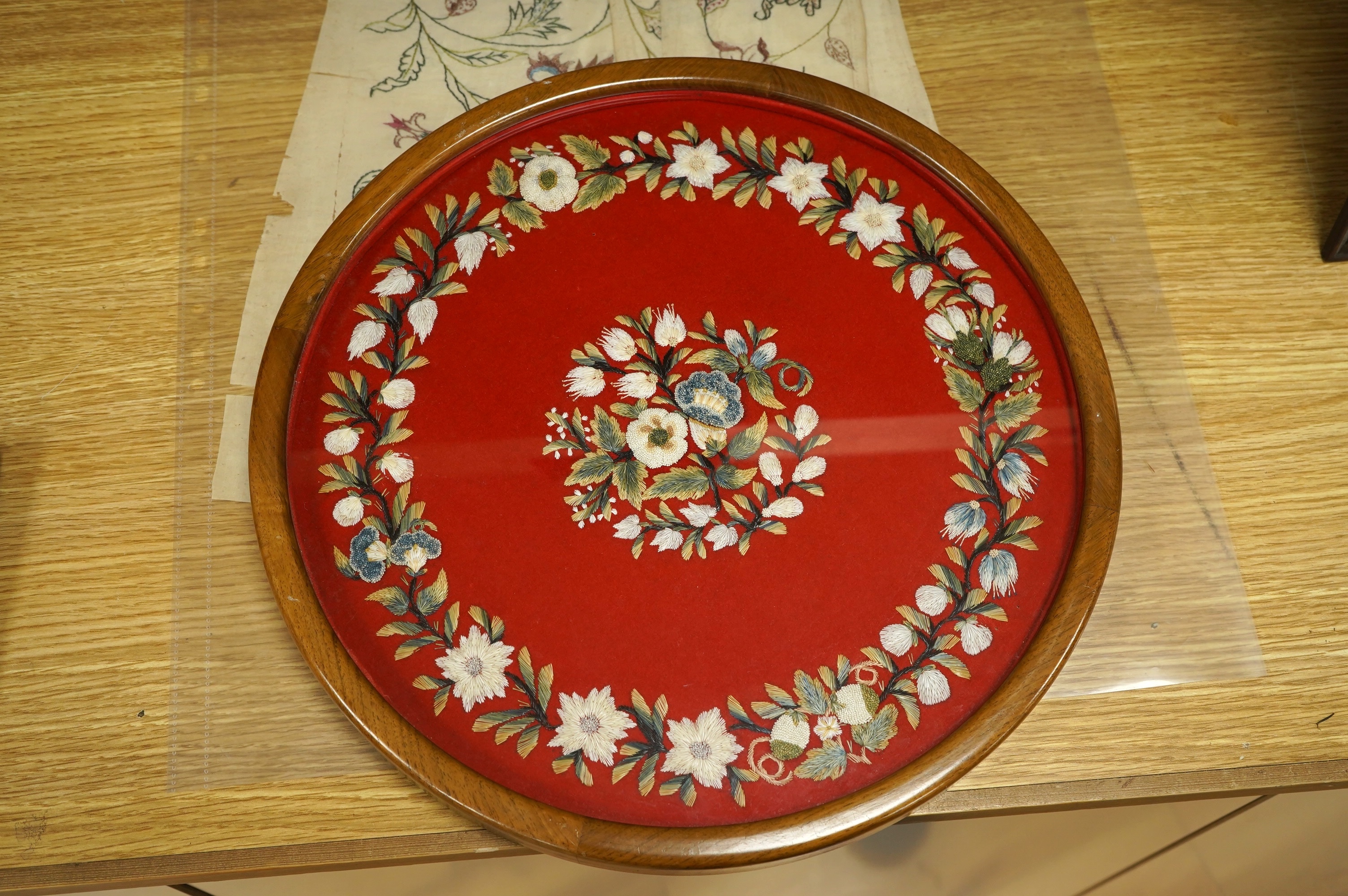 A framed, 19th century, possibly Scandinavian, red felt circular multi-coloured silk embroidery of flowers, acorns and leaves, also embroidered with fine stump work style beadwork flower detail, 32cm diameter. Condition